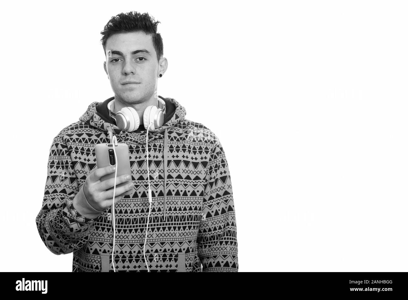 Studio shot of young man holding mobile phone while wearing headphones