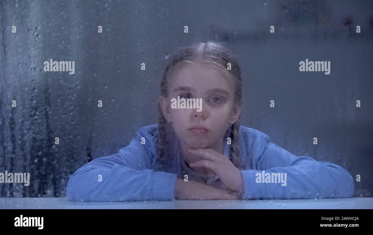 Upset girl looking through rainy hospital window, feeling lonely and insecure Stock Photo