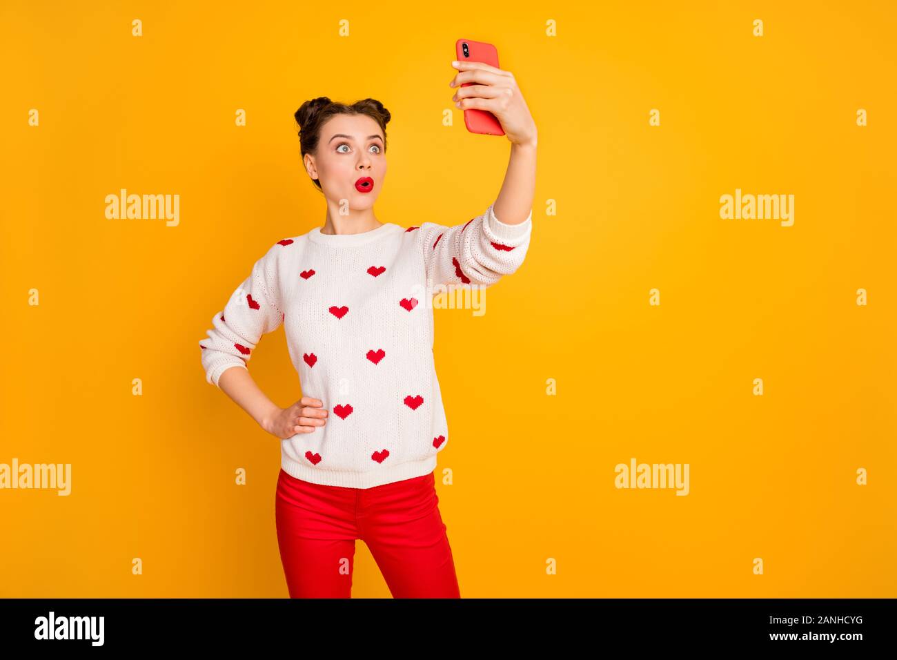 Photo of pretty terrified lady hold telephone hands taking selfies talking skype friends listen bad news wear hearts pattern white pullover red pants Stock Photo
