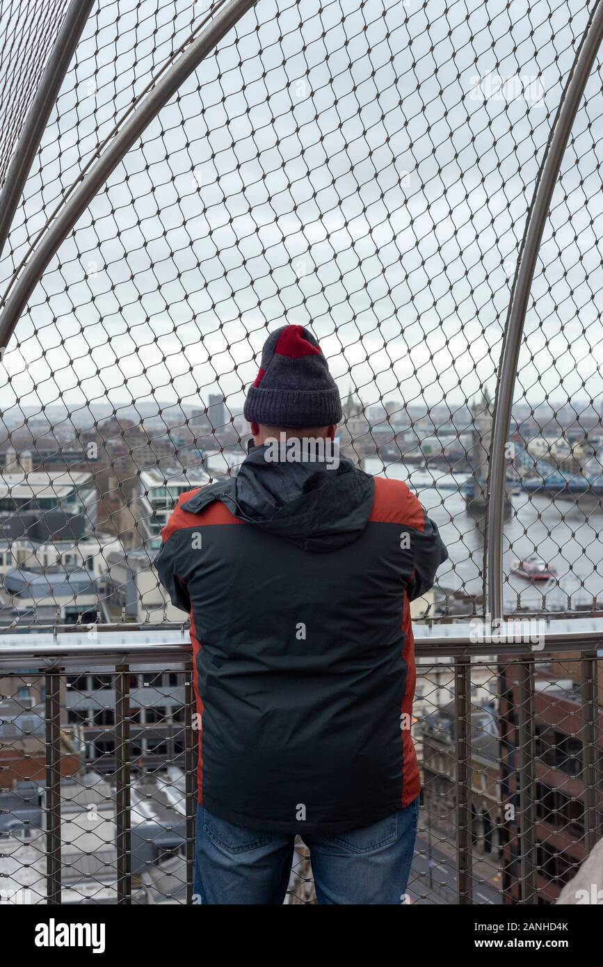 Lone male tourist at the Monument London viewing platform enjoying the view over River Thames and taking photos of Tower Bridge, London, UK Stock Photo