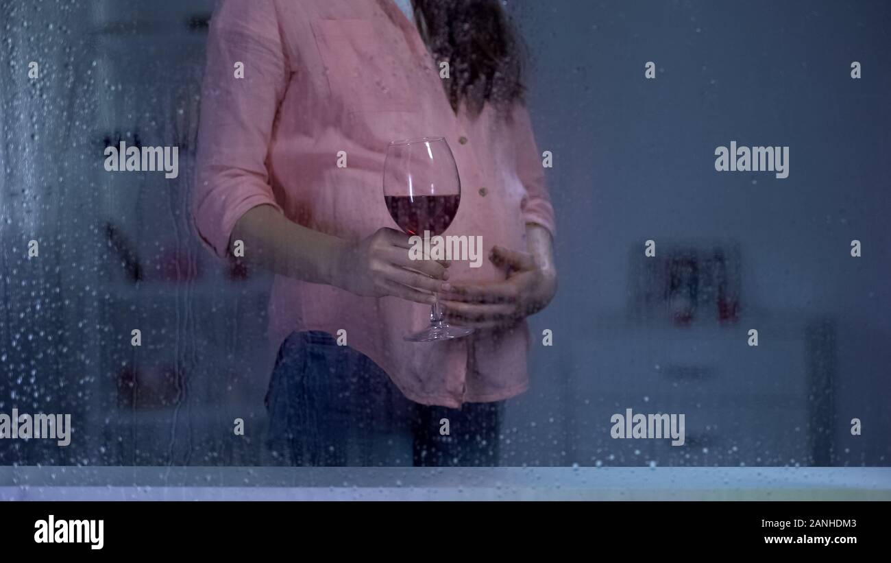 Pregnant woman stroking tummy and drinking wine on rainy day, unwanted baby Stock Photo