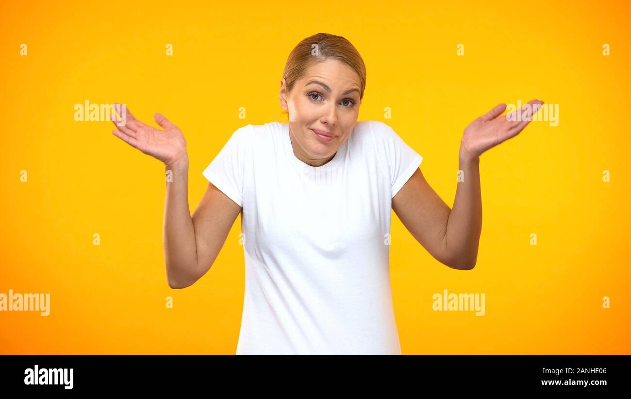 Doubtful woman throwing up hands on bright background, having no idea