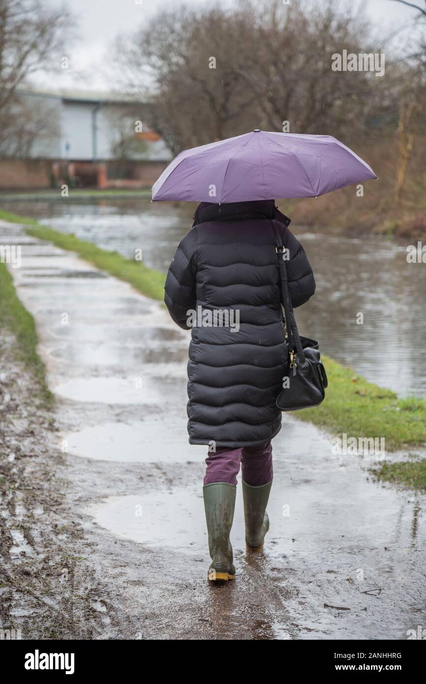 Kidderminster, UK. 17th January, 2019. UK weather: with absolutely no let up in the wet weather, water levels are on the rise and even pavements are flooded forcing pedestrians to resort to their wellington boots. A woman with umbrella, low angle and rear view, is seen here isolated walking through the puddles in her wellies along a canal towpath in the rain. The month of January is proving to be a wet, dreary start to the new year. Credit: Lee Hudson/Alamy Live News Stock Photo