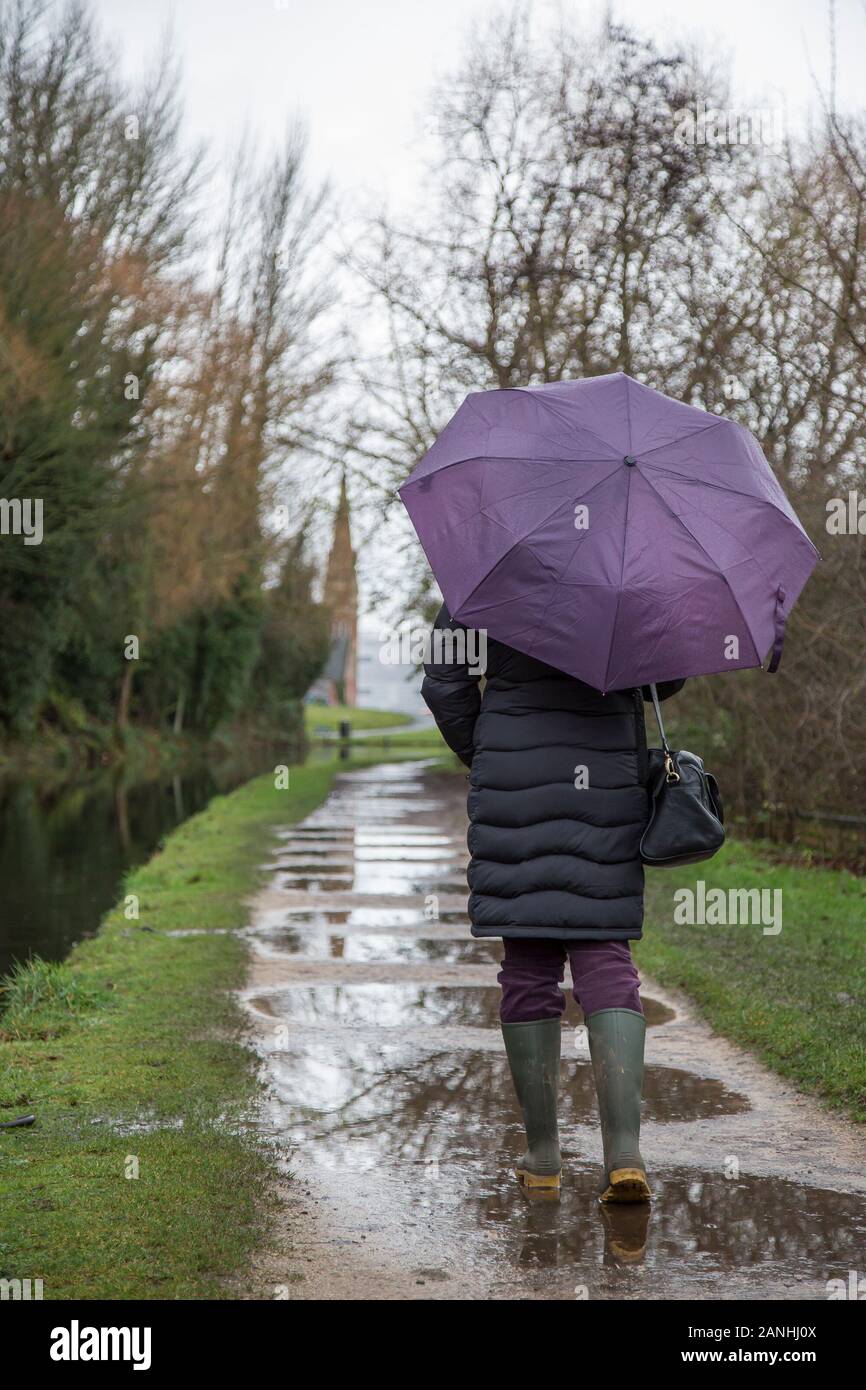 Kidderminster, UK. 17th January, 2019. UK weather: with absolutely no let up in the wet weather, water levels are on the rise and even pavements are flooded forcing pedestrians to resort to their wellington boots. A woman with umbrella, rear view, is seen here isolated walking through the puddles in her wellies along a canal towpath in the rain. The month of January is proving to be a wet, dreary start to the new year. Credit: Lee Hudson/Alamy Live News Stock Photo