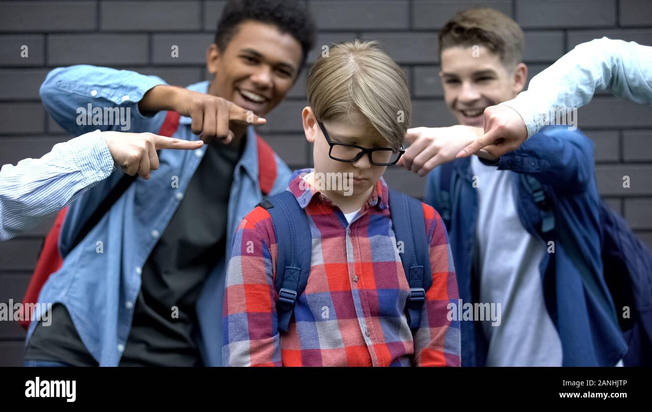 Evil schoolchildren pointing fingers at junior boy, mocking nerd, bullying Stock Photo