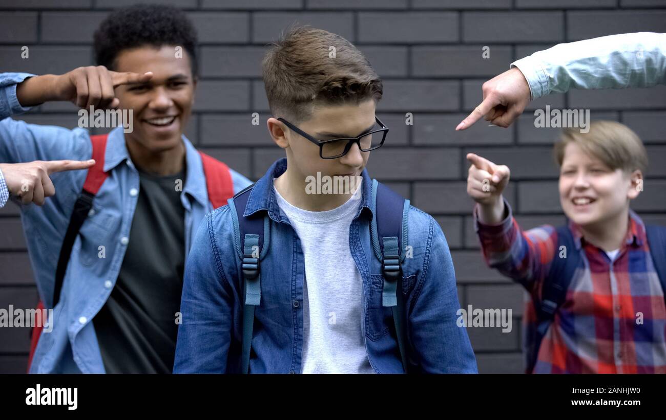 Cruel schoolchildren pointing fingers at student, mocking smart boy, bullying Stock Photo