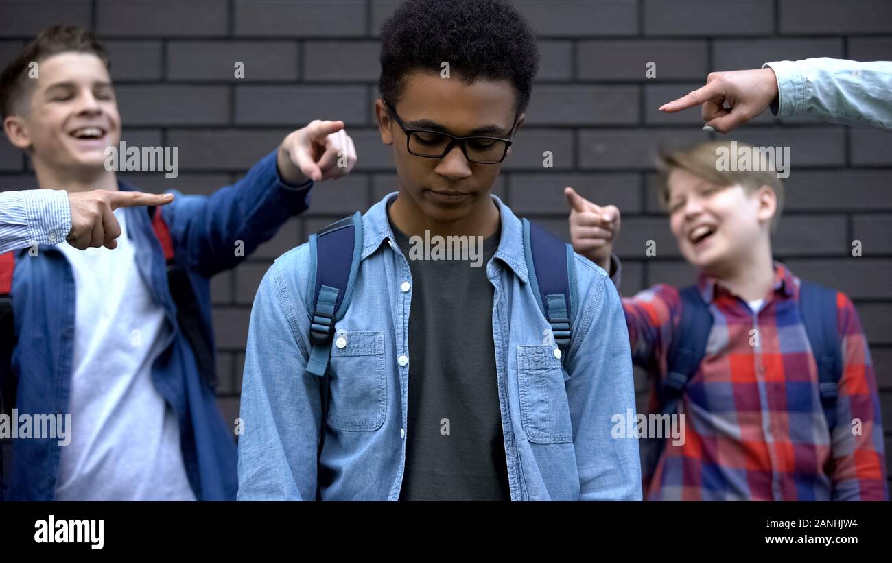 Group of cruel teenagers pointing fingers at black boy, humiliation and racism Stock Photo