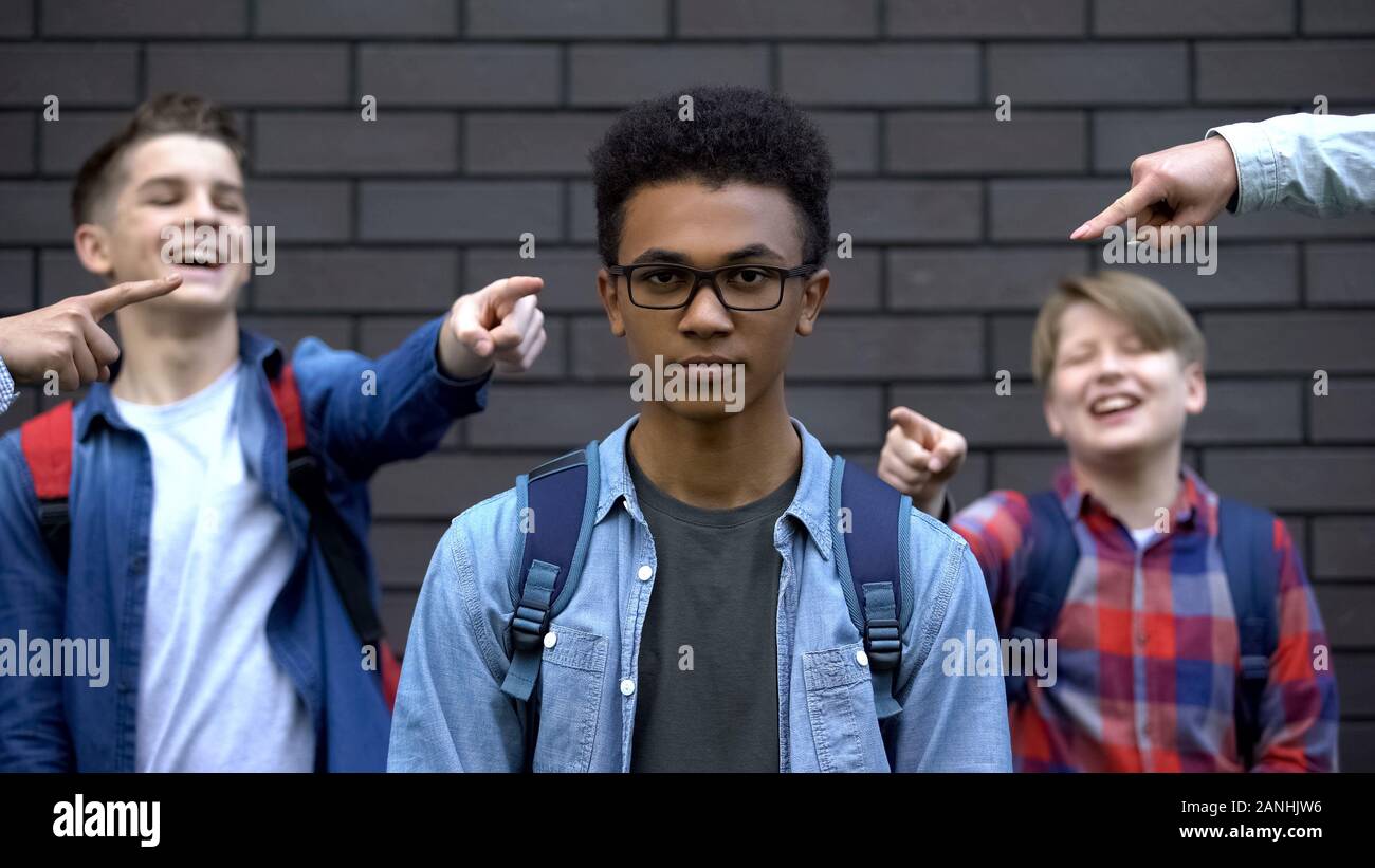 Group of teenagers pointing fingers and laughing at black boy, racial bullying Stock Photo