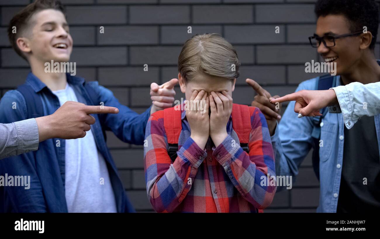 Malicious teenagers pointing fingers at boy crying, depressed victim of bullying Stock Photo