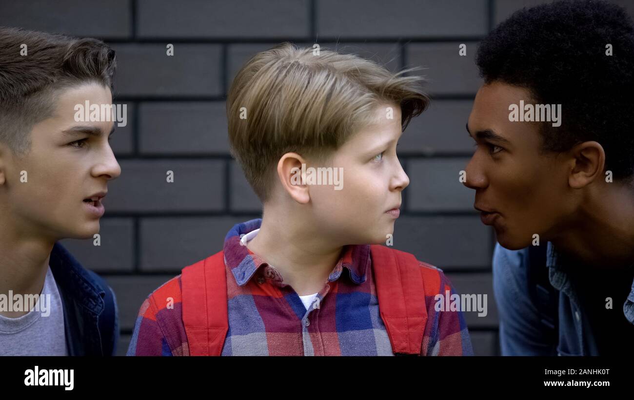 Malicious students teasing boy face-to-face, telling insults, emotional bullying Stock Photo