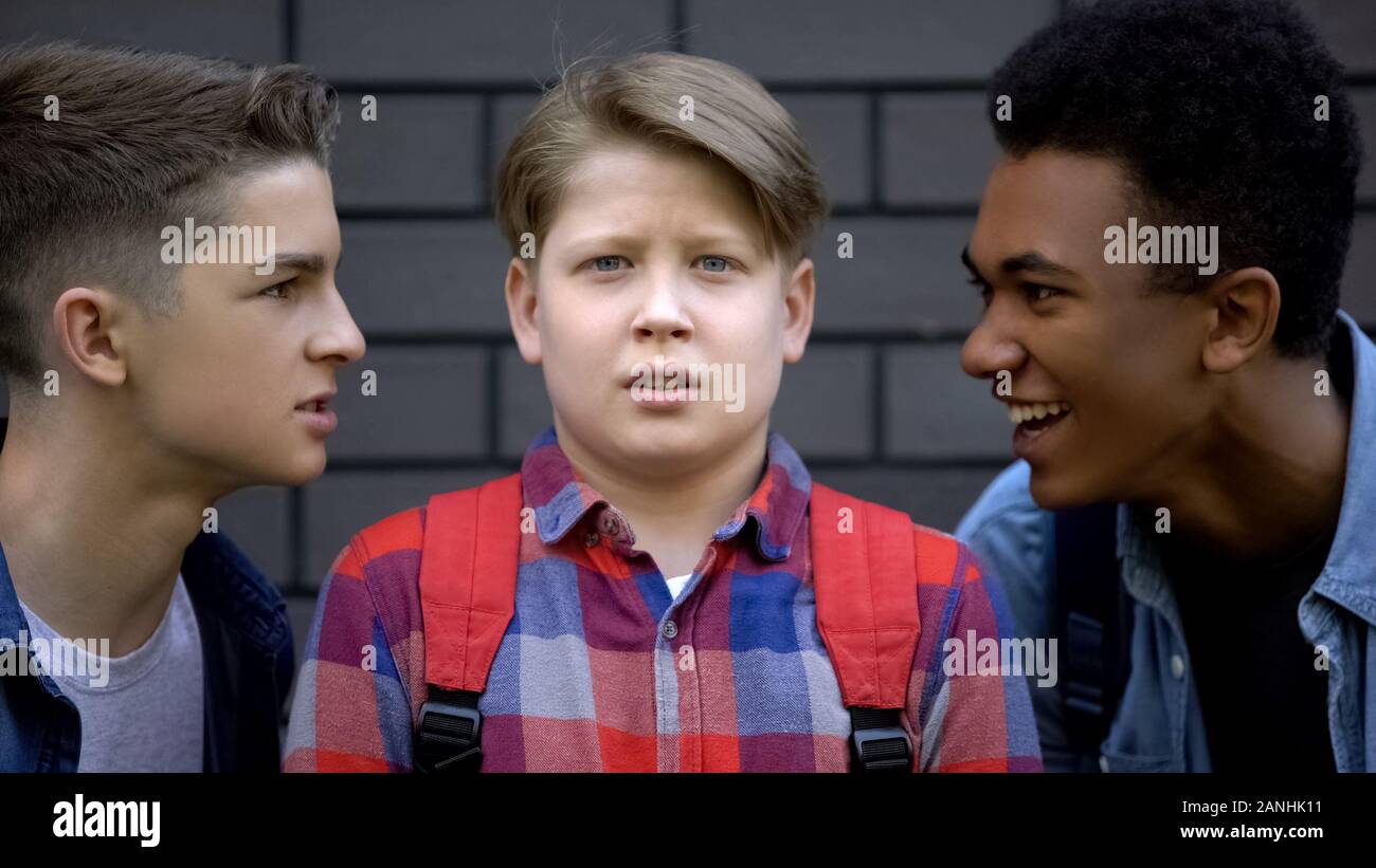 Aggressive students teasing boy face-to-face telling insults, emotional bullying Stock Photo