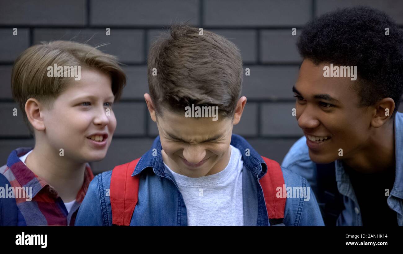 Spiteful students teasing boy face-to-face, telling insults, emotional bullying Stock Photo