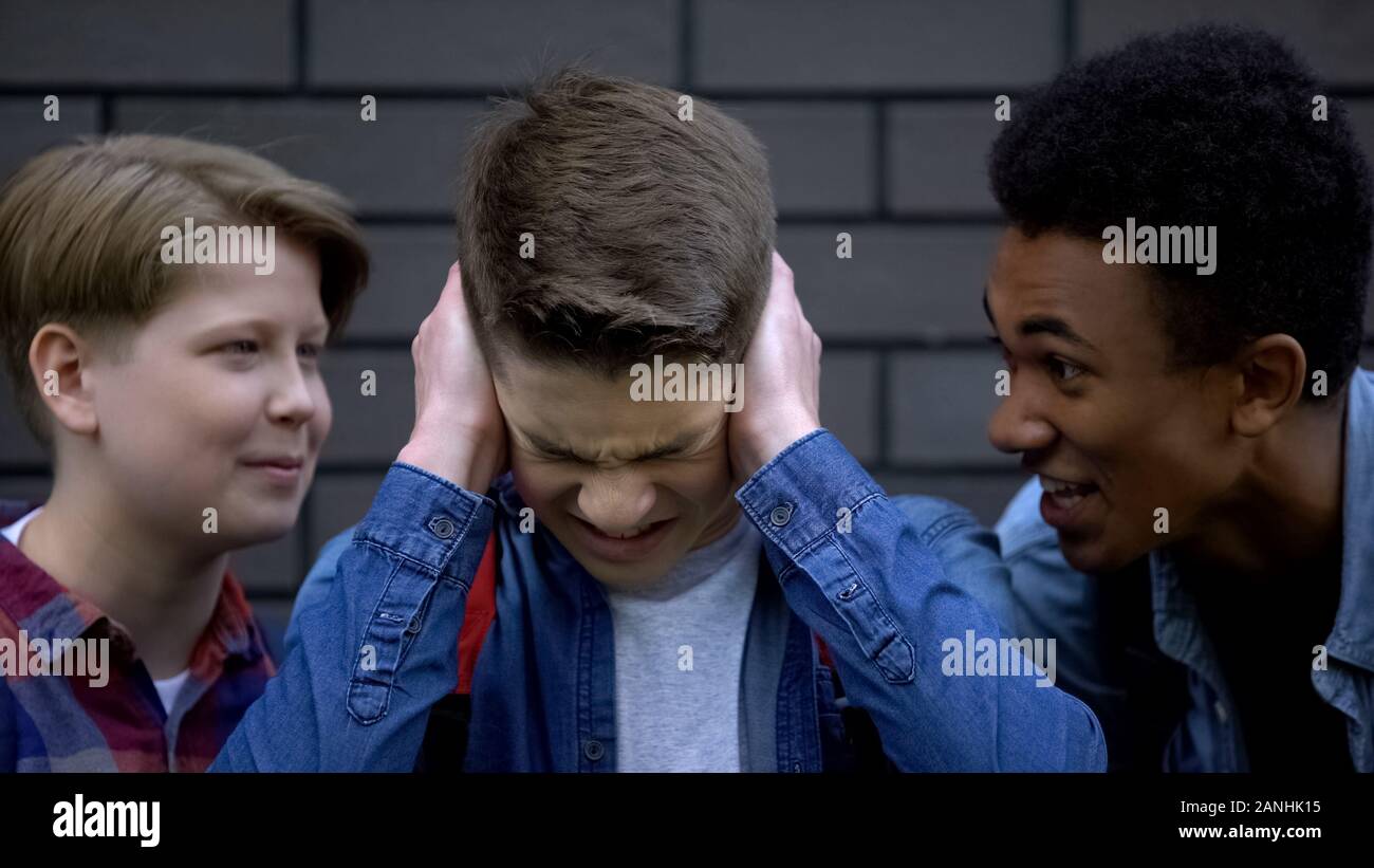 Depressed boy covering ears from mockery and insults of schoolmates, bullying Stock Photo
