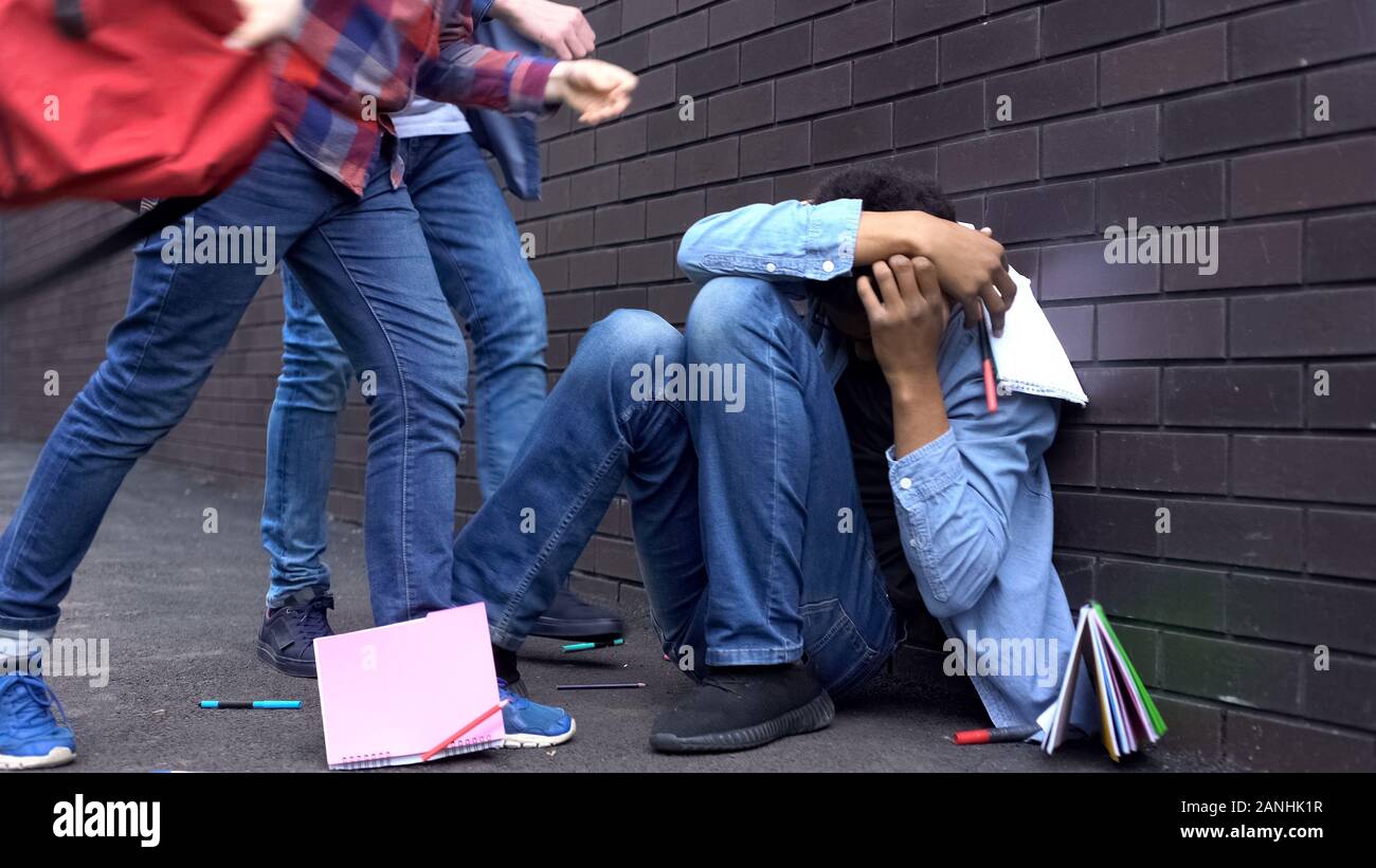 Cruel teenagers scattering classbooks of afroamerican boy, school