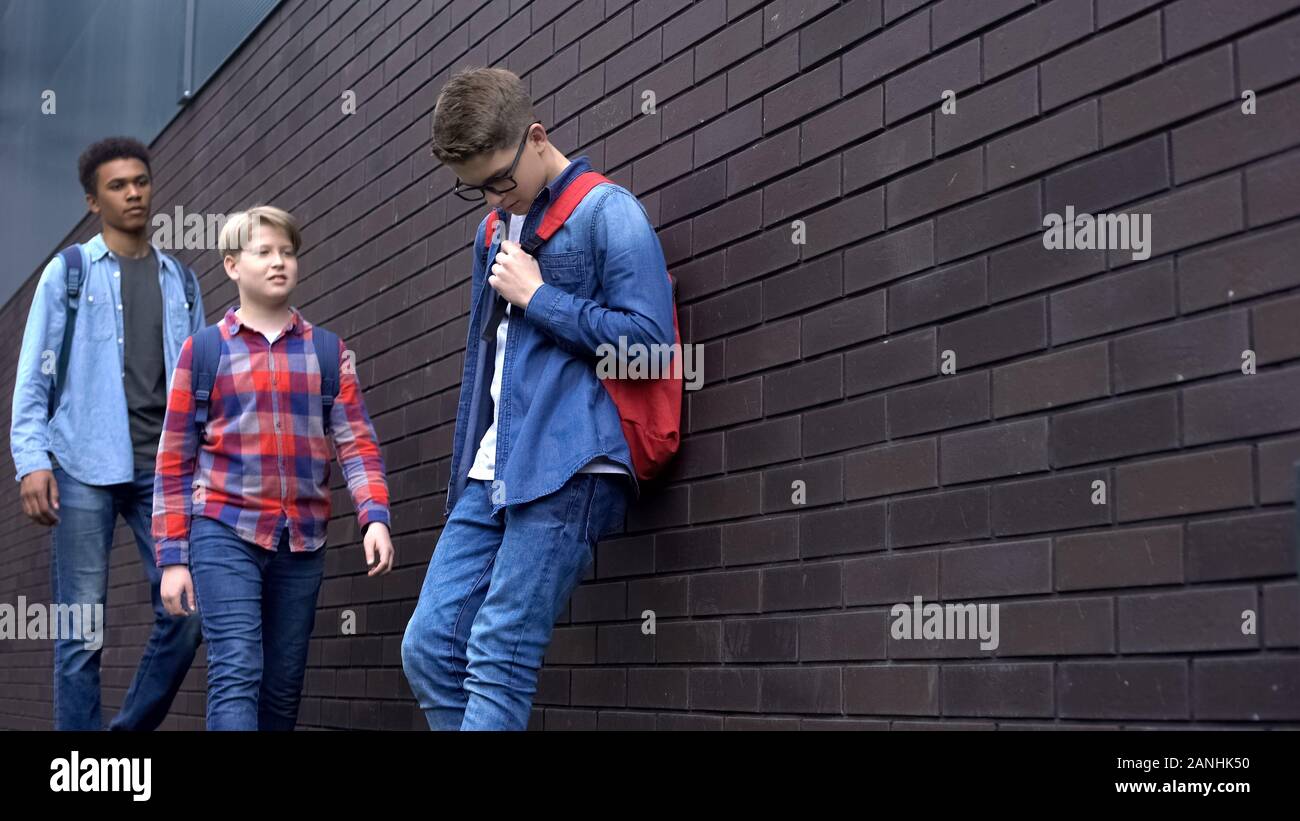 Mean students approaching nerd boy in backyard, school bullying, intimidation Stock Photo