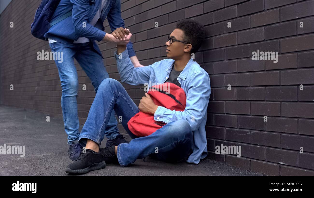 Teenage student giving helping hand to bullied afro-american boy, stop racism Stock Photo