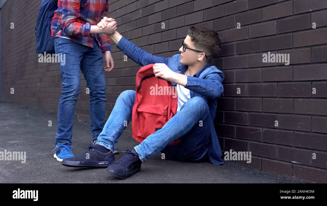 Kind teenage student giving helping hand to bullied nerd boy, supportive friend Stock Photo