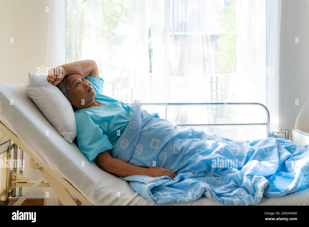 Asian depressed elderly woman patients lying on bed looking out the