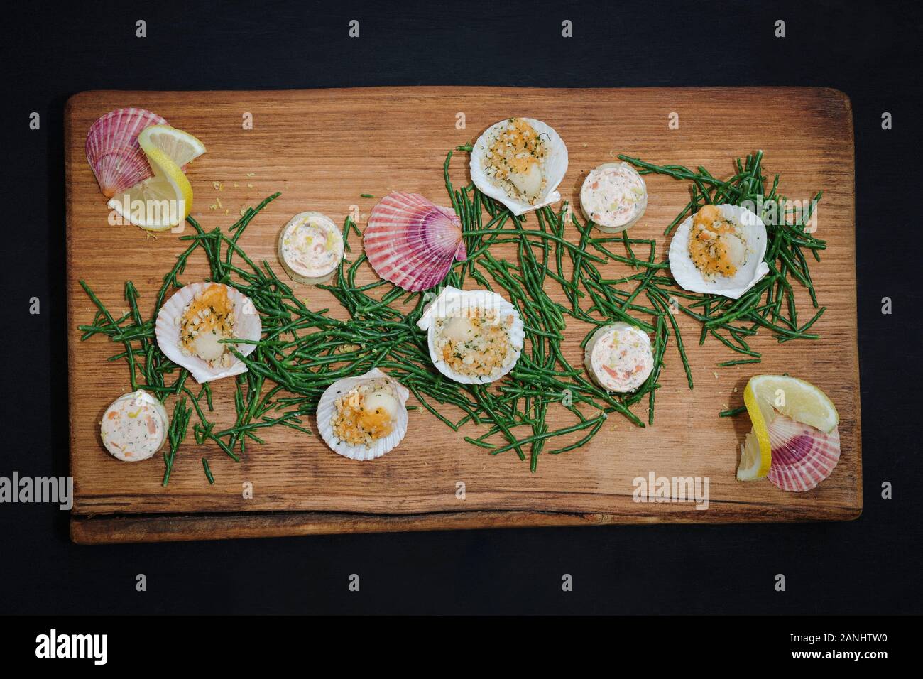 Seafood platter: Canapes served on a wooden board with scallops and samphire and lemon wedges. Top view. Stock Photo