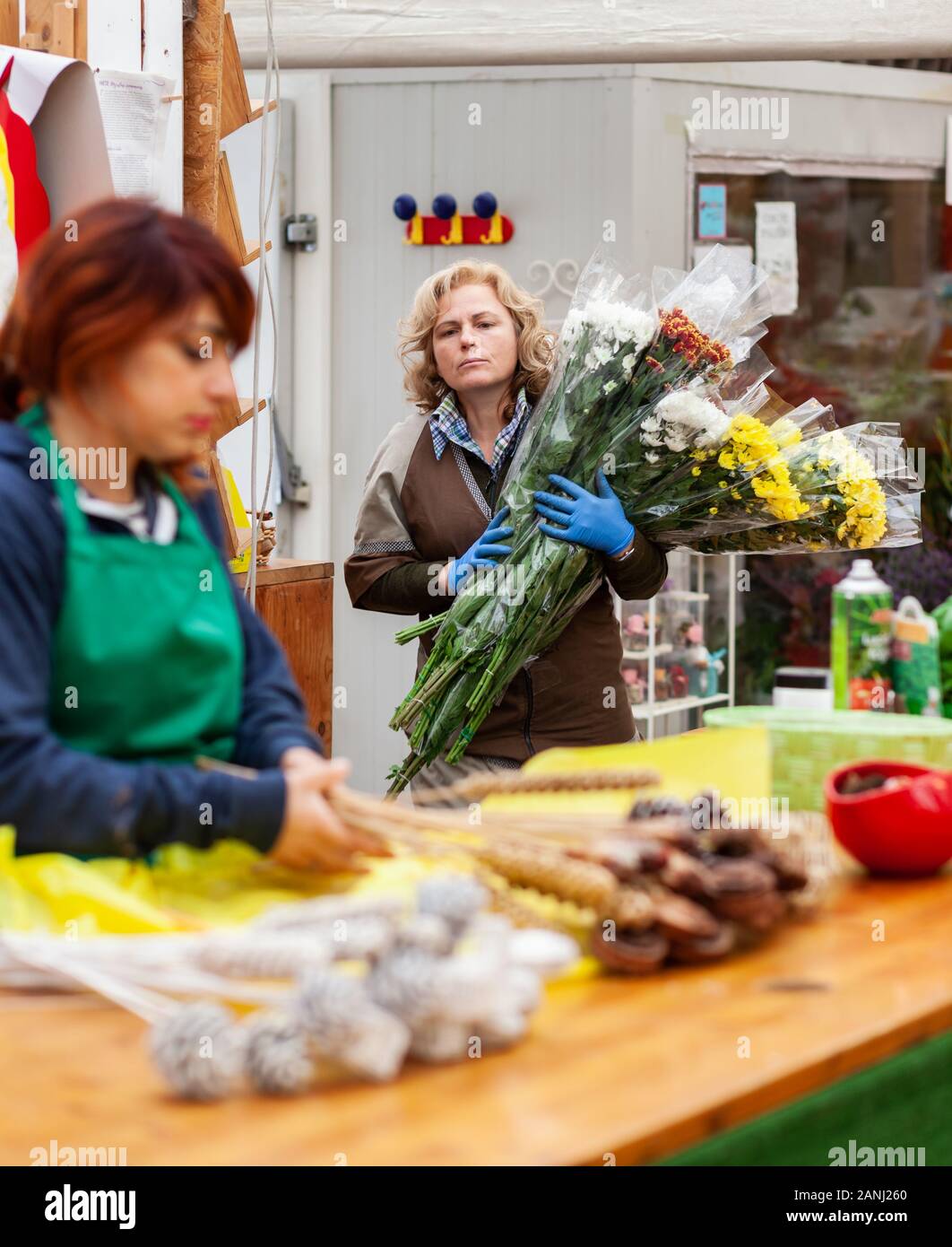 Two florists work in a nursery. Couple work in the gardening business on an ordinary working day. In the photo a blonde woman and a young woman with r Stock Photo