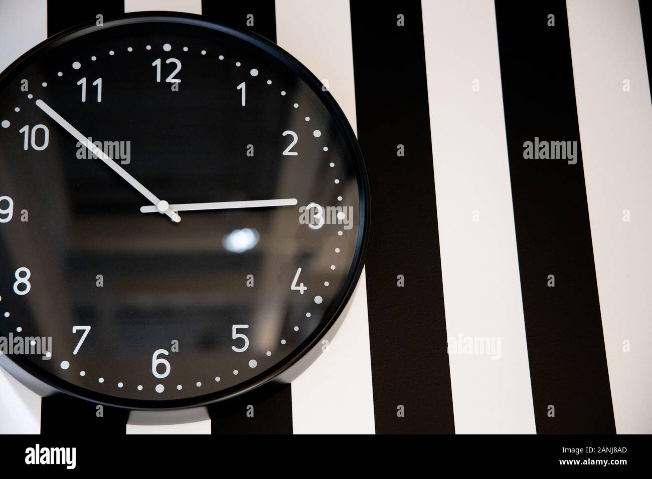 large black clock on the striped wall of the room Stock Photo Alamy