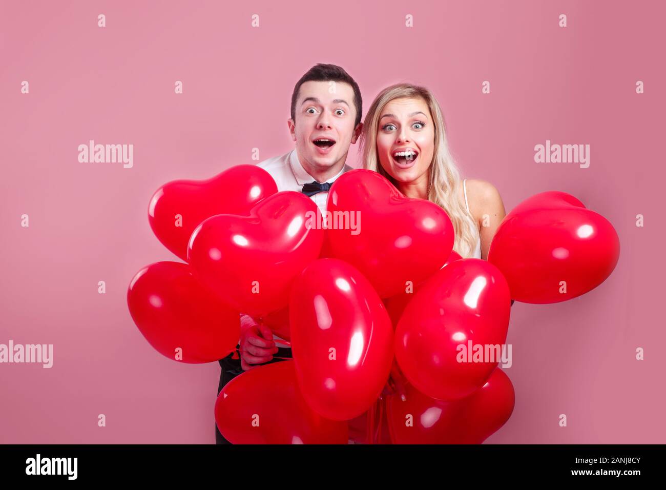 Funny surprised young couple with balloons heart on pink background ...