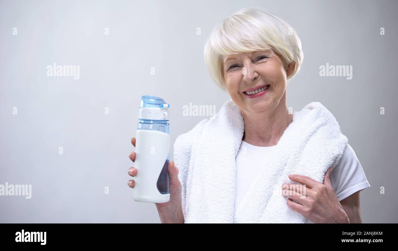 Energetic old woman with towel holding isotonic water, sport nutrition, health Stock Photo