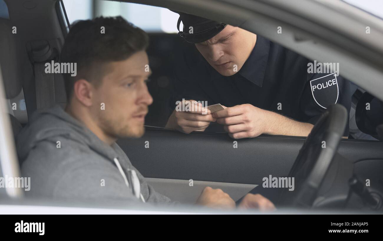Strict policeman checking male drivers license after exceeding speed