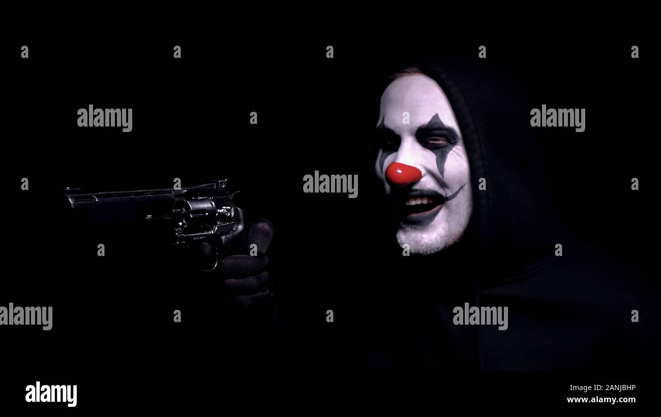 Contract killer in clown face mask aiming gun, crazy robber intimidating victim Stock Photo