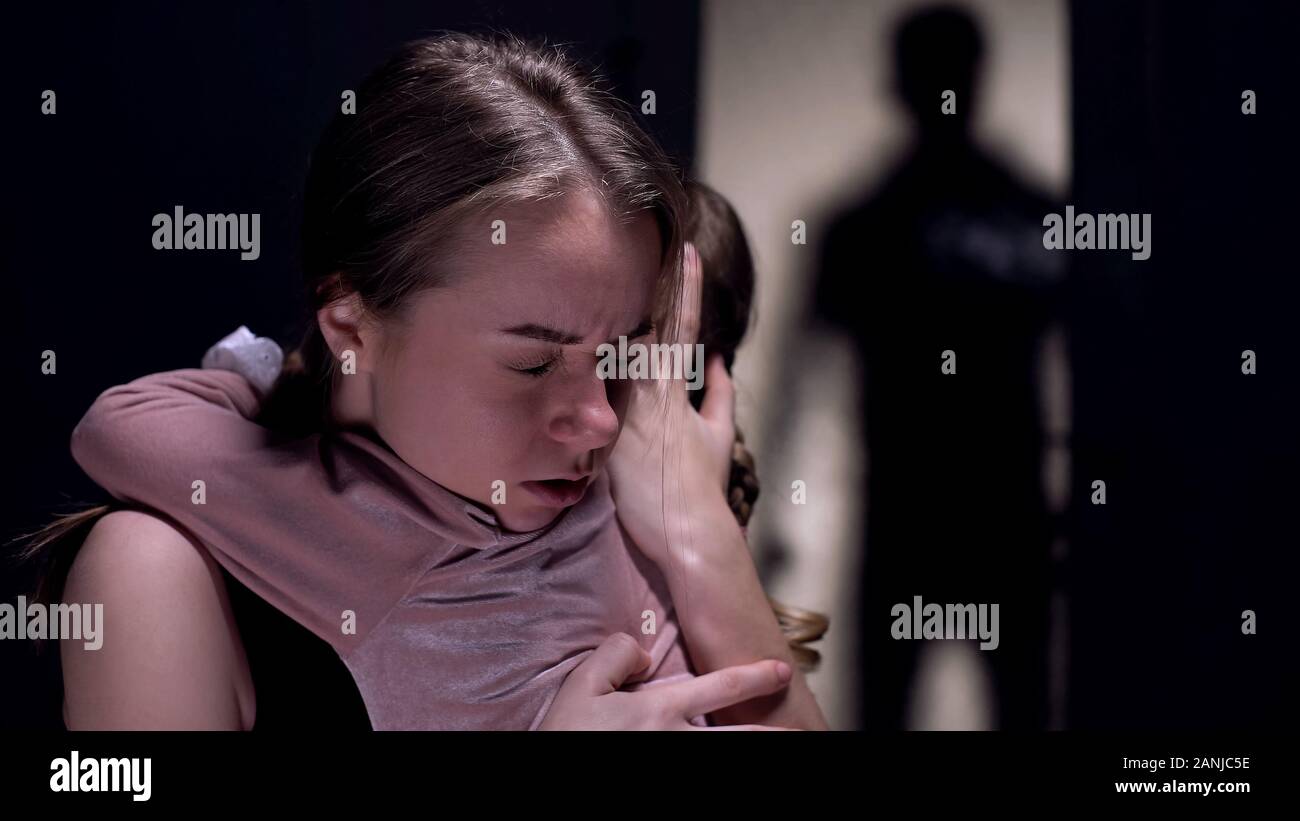 Frightened mother hugging daughter, felon shadow entering room, crime witness Stock Photo