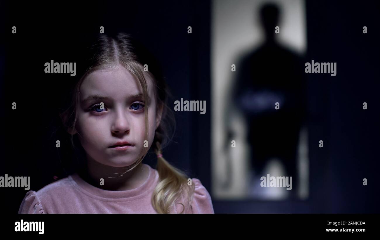 Frightened female kid crying on camera shadow of tyrant father with belt outside Stock Photo