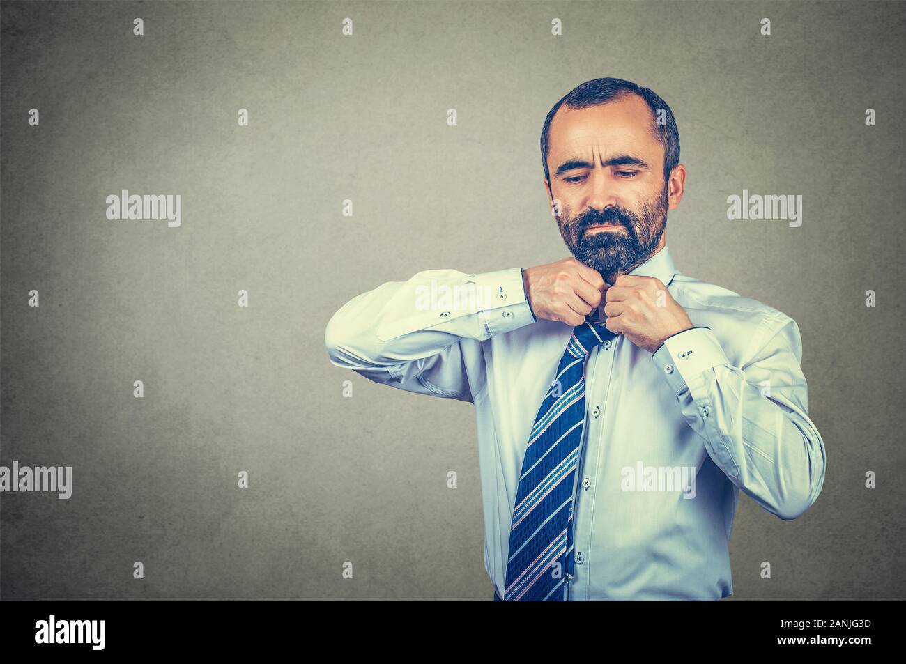 Closeup portrait of tired businessman taking off his tie off. Mixed race bearded model isolated on gray studio wall background with copy space. Horizo Stock Photo
