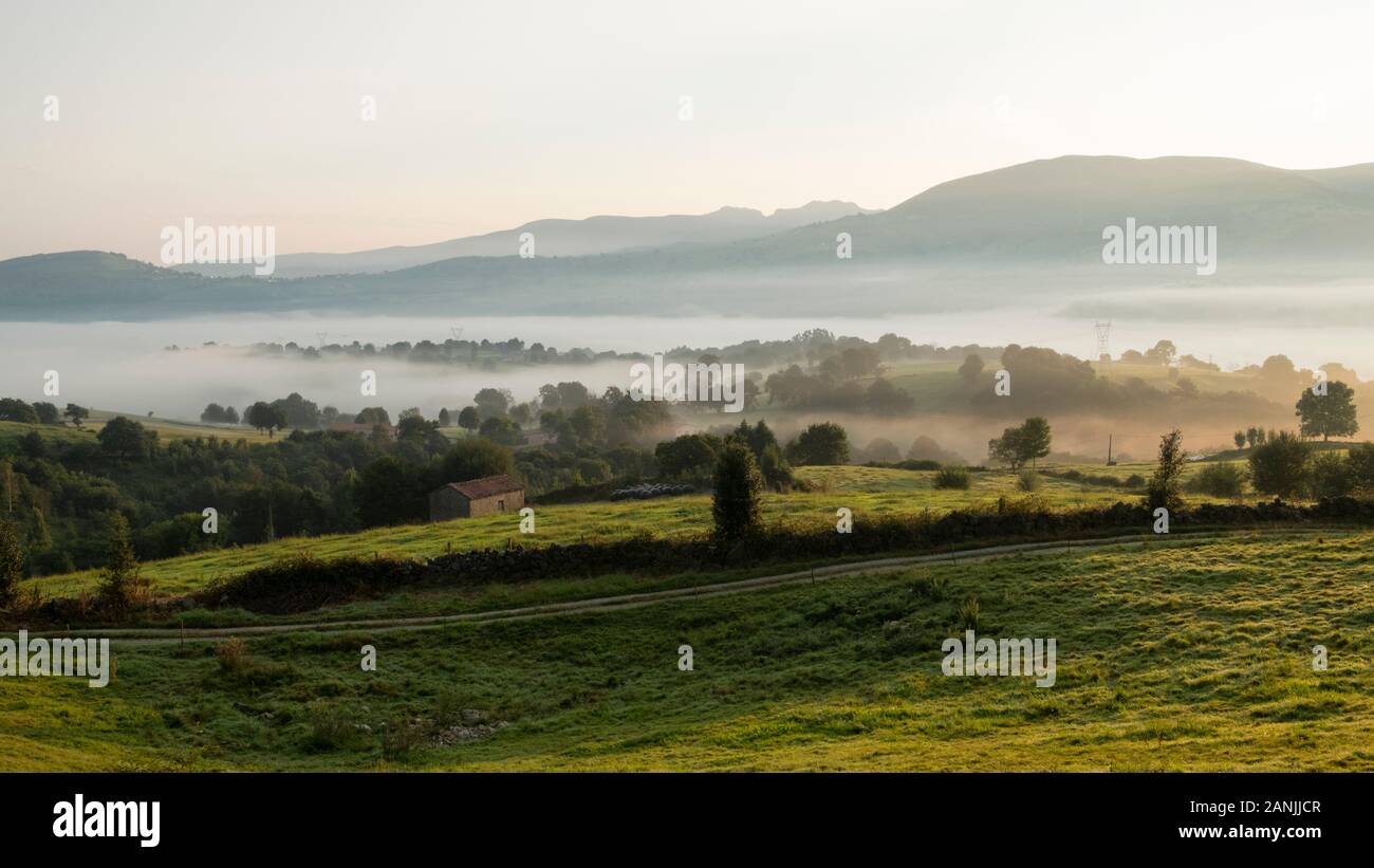 Traditional cabaña pasiega hut and pastures in Valles Pasiegos countryside covered with mist at sunrise (Tezanos, Villacarriedo, Cantabria, Spain) Stock Photo