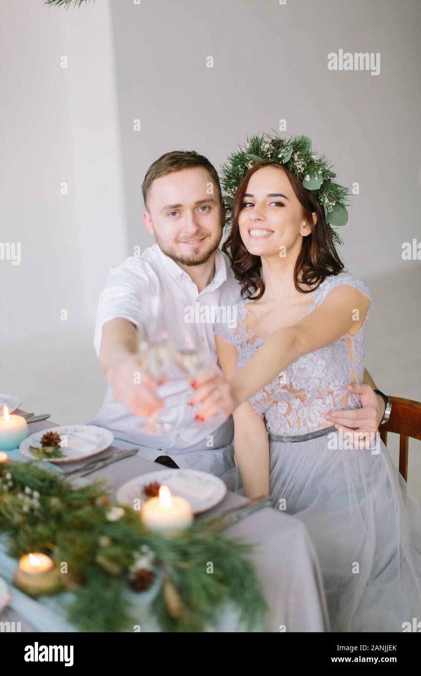 Happy bridesmaid and groomman at the wedding table drink champagne. Group of people sitting at wedding table in the white hall decorated with pine Stock Photo