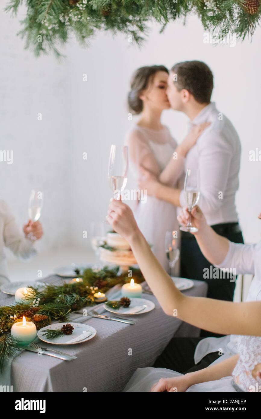 Bride And Groom kissing and Enjoying Meal At Wedding Reception. Guests drink champagne at the wedding table decorated with pine and candles Stock Photo