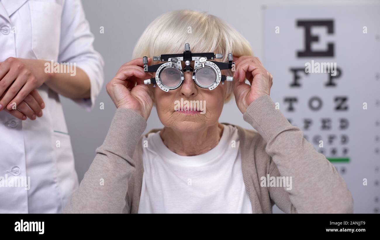 Doctor putting phoropter on elderly woman eyes, choosing proper lens diopter Stock Photo