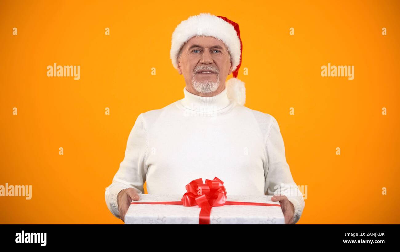 Positive elderly man in Santa hat holding gift box, best presents shop ad Stock Photo