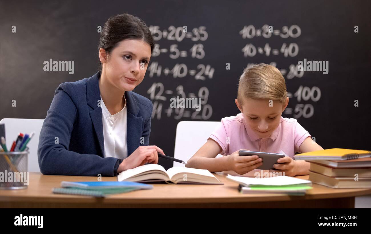 Strict teacher waiting naughty boy finishing playing on smartphone to teach him Stock Photo