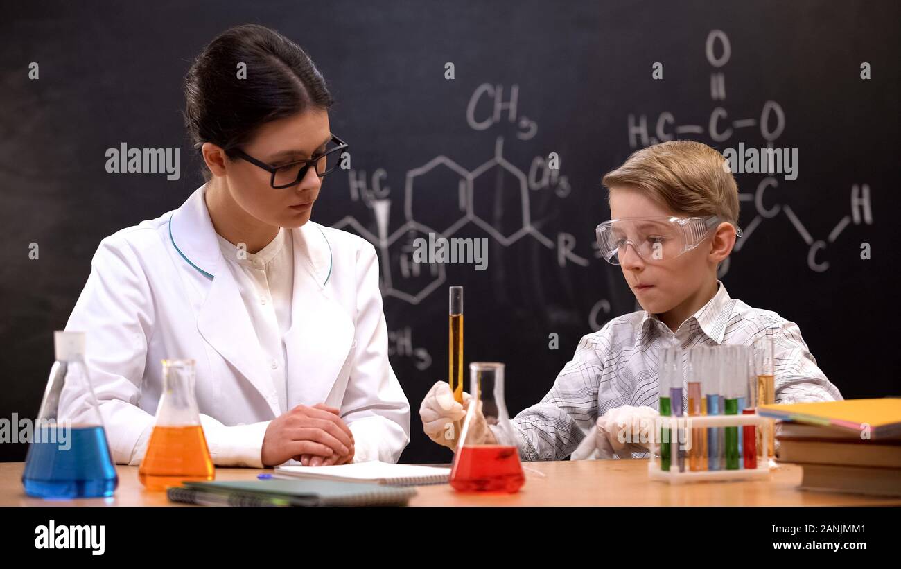 Schoolboy holding test tube with orange liquid observing reaction with teacher Stock Photo
