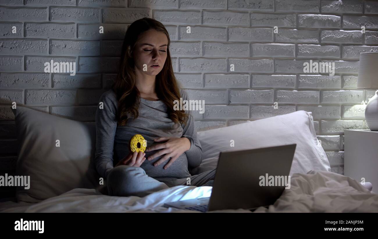 Pregnant woman holding doughnut and watching film, unhealthy nutrition concept Stock Photo