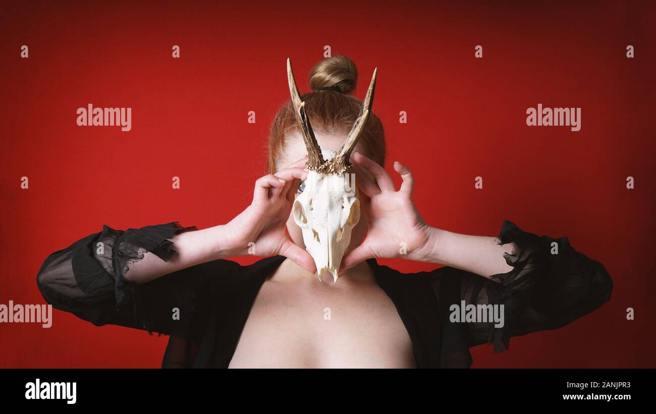 mysterious occult woman holding animal deer skull in front of her face - animalism witch or sorceress Stock Photo