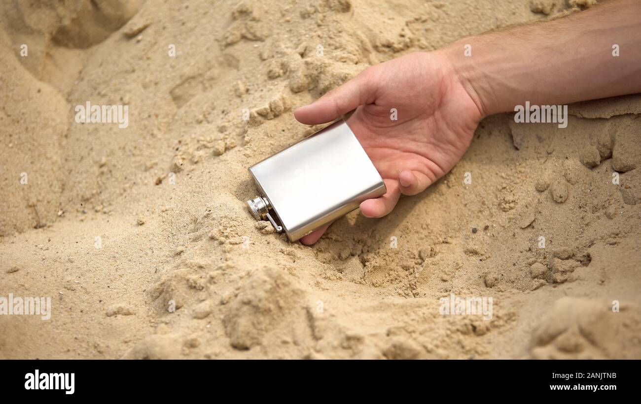 Hand with flask lying lifeless on sand, deadly effects of alcohol addiction Stock Photo