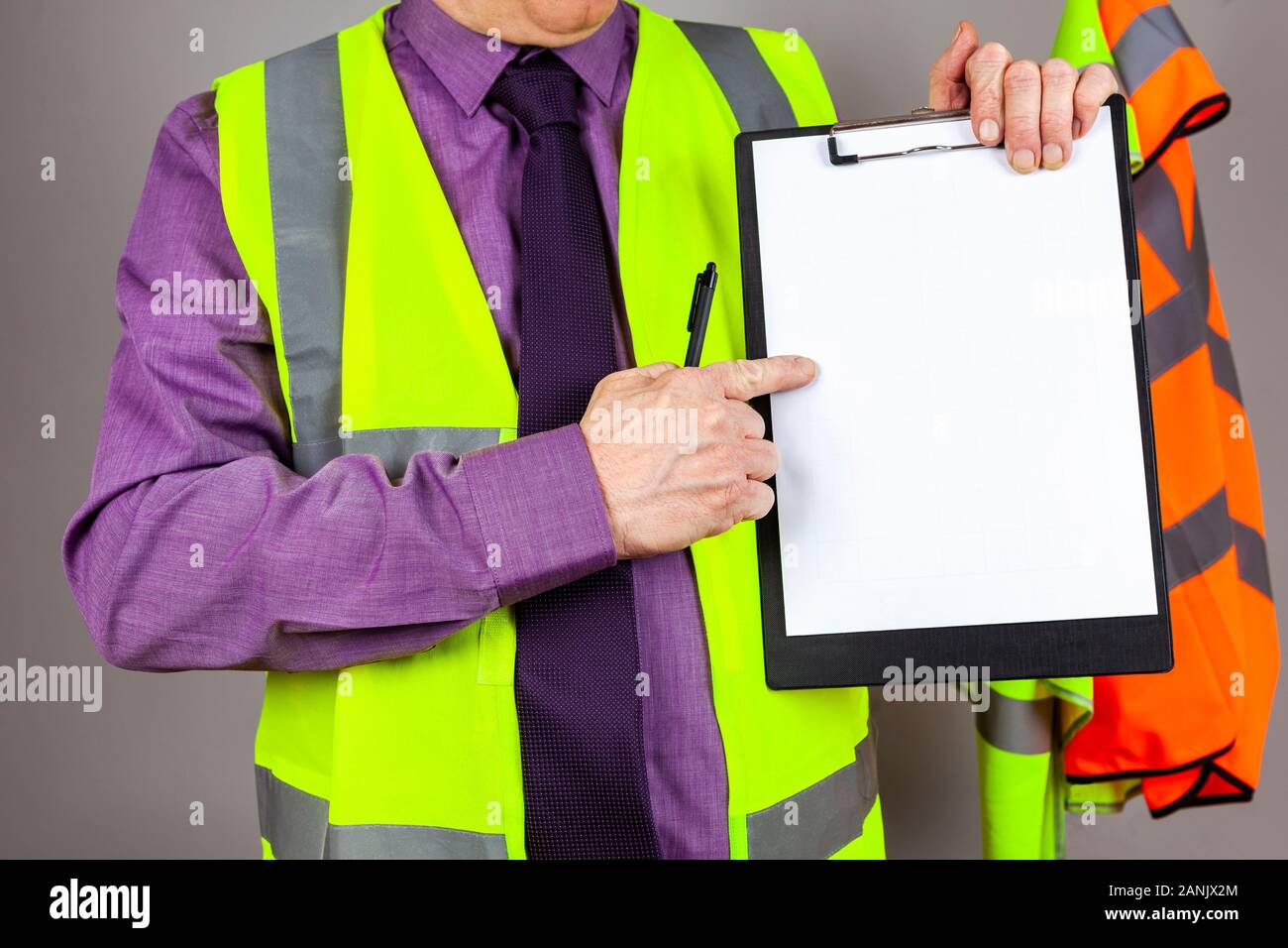 Health and safety instructor in a yellow high visibility vest pointing at a blank sheet of white paper on a black clipboard Stock Photo