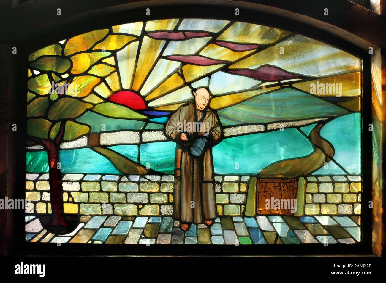 Coloured glass window depicting a friar with a sunny landscape behind ...