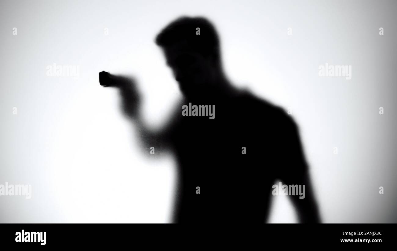 Shadow of male killer aiming gun through glass wall, contract murder, crime Stock Photo