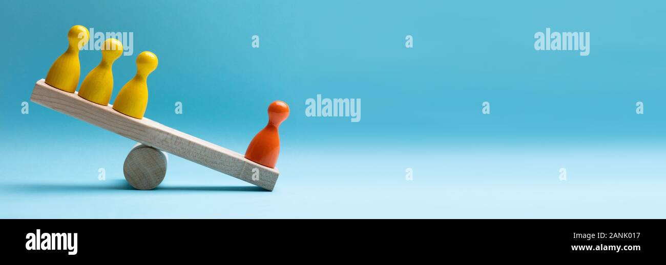 Close-up Of Pawns Figures Balancing On Wooden Seesaw Over Blue Surface Stock Photo