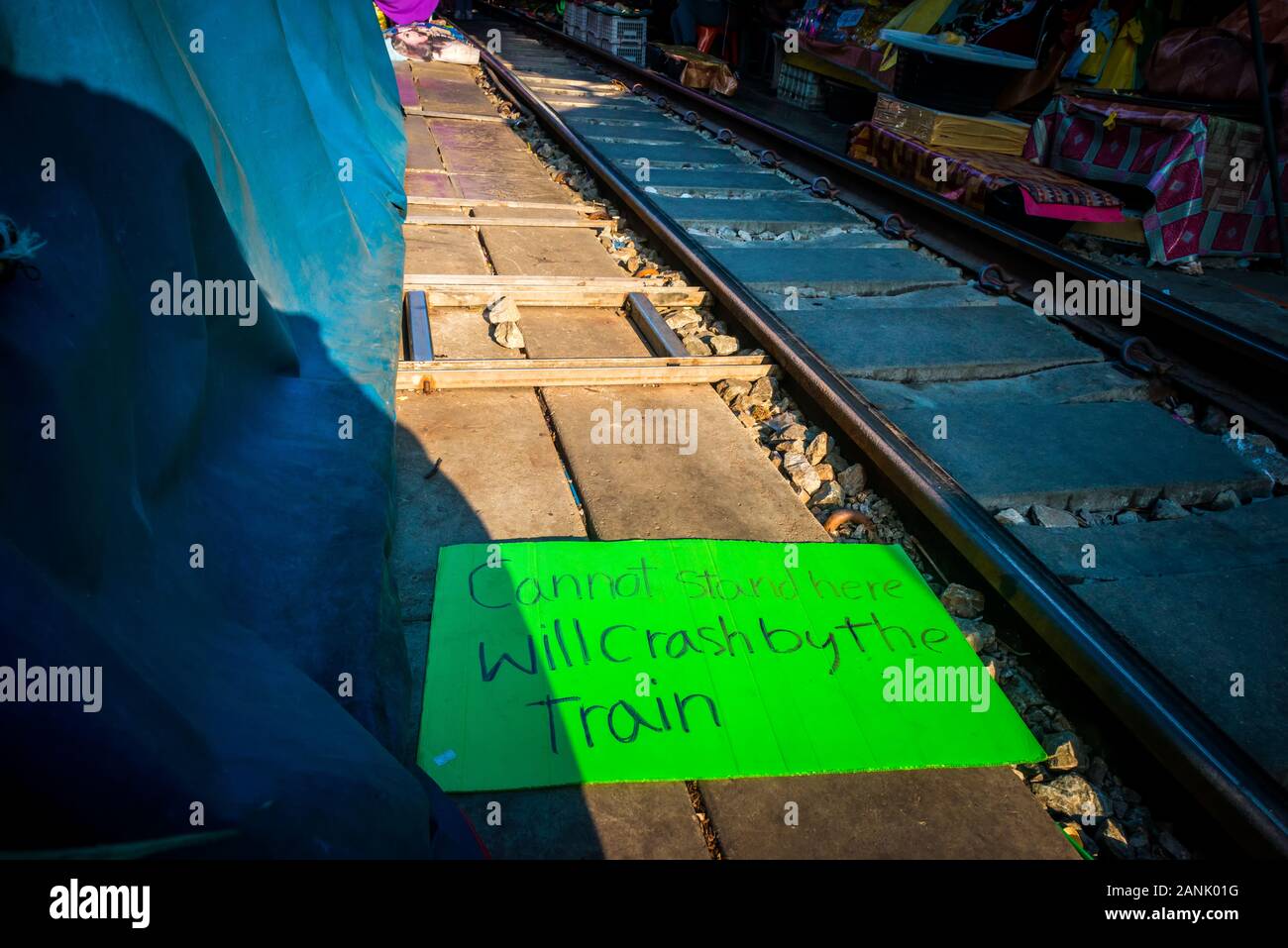 Mae Klong/Thailand-08December2019: Mae Klong train station with tracks and train passing through and a sign saying 'train will crash you' Stock Photo