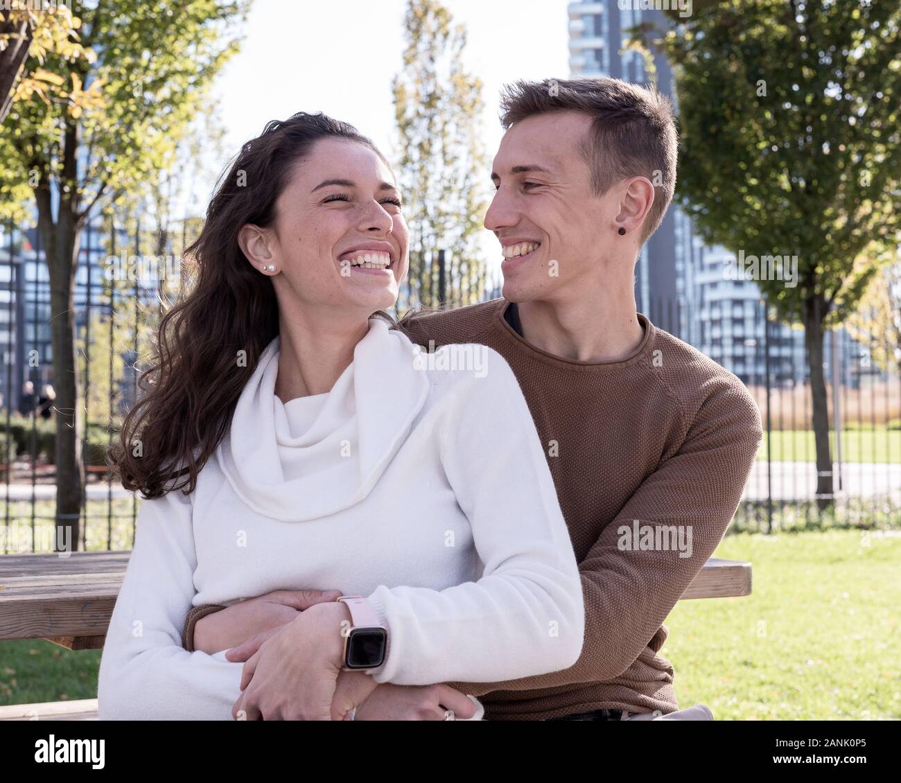 A couple in love millenials hugging each other on a bench and laughing with joy, outdoor couple life, love concept Stock Photo