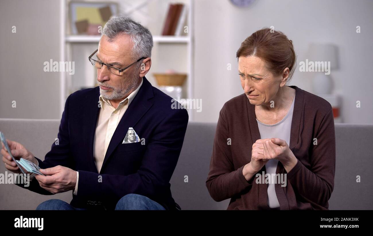 Desperate needy female looking at wealthy gentleman counting dollars, poverty Stock Photo