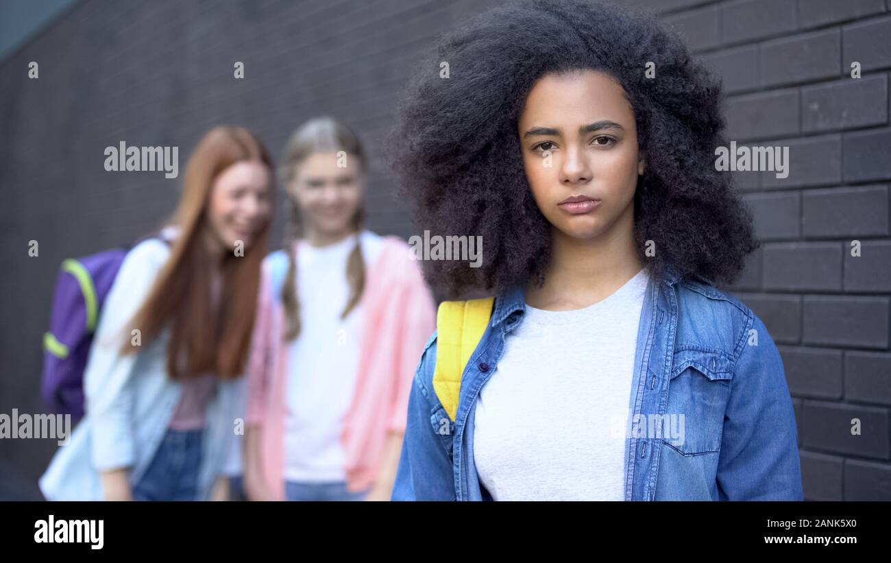 Sad bullying victim looking camera, female classmates teasing african schoolgirl Stock Photo